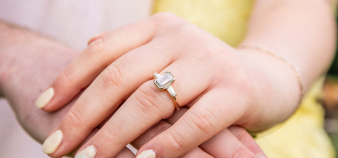 Vintage-inspired emerald cut engagement ring with baguette side stones shown on hand in yellow gold